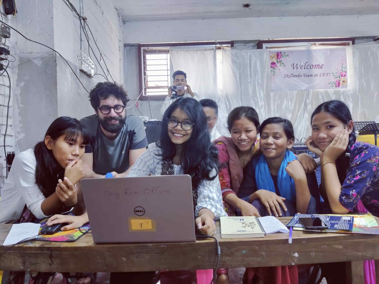 Un volontario di Skillando insieme a ragazzi locali, impegnati in un project work al computer, collaborando su un'attività di gruppo.