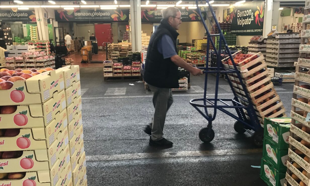 Un uomo con un carrello carico di pesche si muove in un'area di mercato.