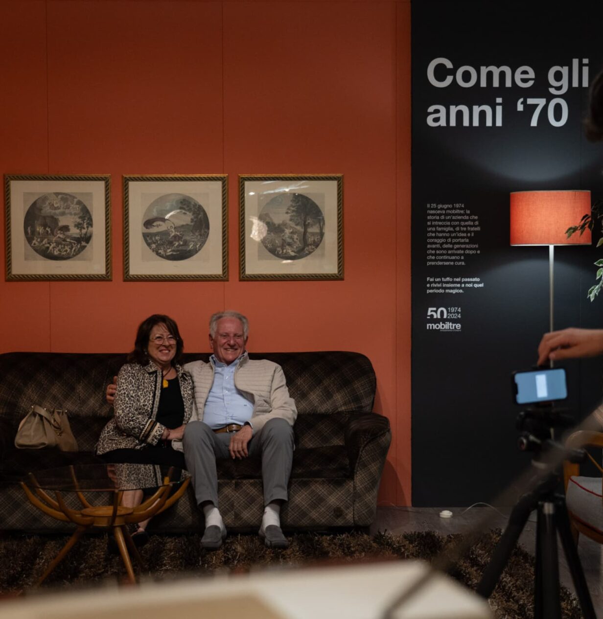 Una signora e un signore seduti su un divano vicino alla parete espositiva di mobiltre.