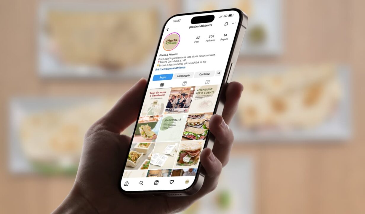 Mano che tiene uno smartphone aperto sul profilo Instagram di "Piada & Friends". Il feed presenta contenuti legati alle piadine e agli ingredienti.