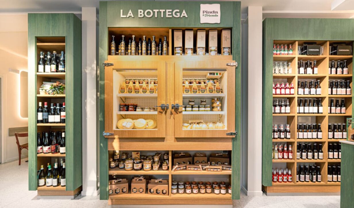 Interni di "Piada & Friends" in legno verde chiaro con scaffali di vino, prodotti gastronomici e formaggi.