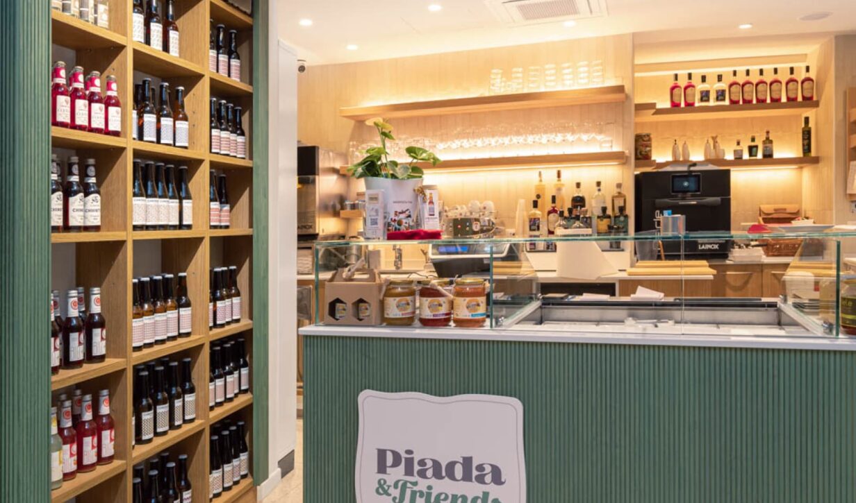 Interno del locale "Piada&Friends" con bancone e scaffalature in legno con bottiglie e prodotti.