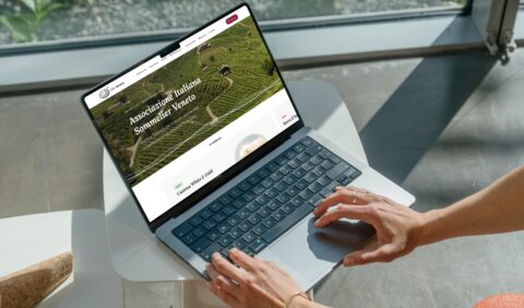 Persona che utilizza un laptop su un tavolo, con il sito AIS Veneto aperto, mostrando vigneti e corsi sul vino.